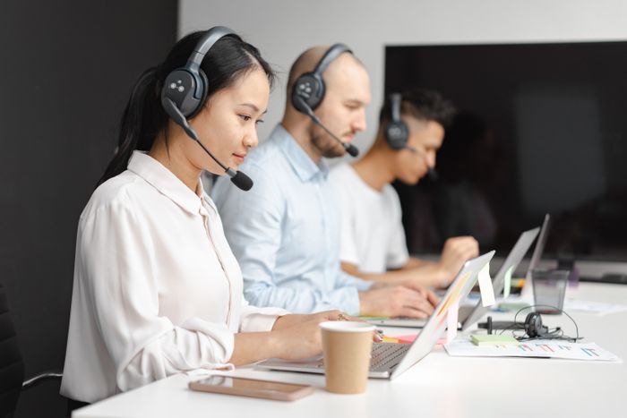 Row of call center agents wearing headsets working on laptops